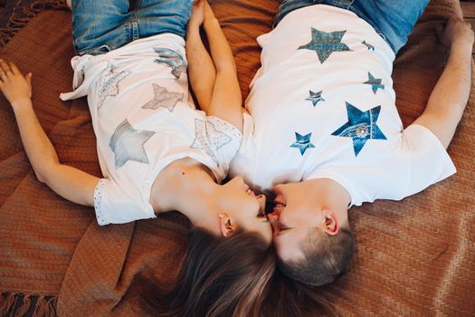Above view of young couple laying together in bed at studio. Two people smiling and holding hand, spending time together and having fun, wearing in white t-shirt. Concept of love and relationship.