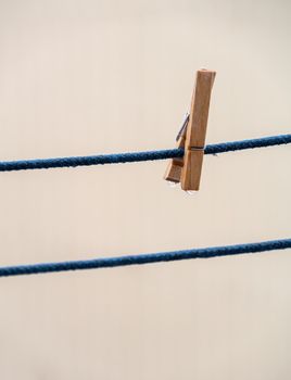 One wooden clothespin on a blue rope with hanging waterdrops after the rain on blurred background. Wet clothesline with clothes clip.