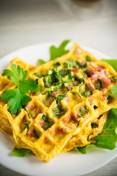 Egg omelet stuffed with greens and sausage fried in the form of waffles, on a wooden table