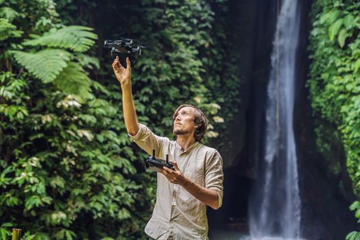 The man controls the drone against the background of the forest and the waterfall.