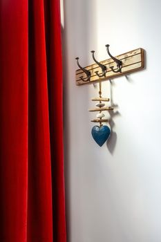Wooden vintage style hanger with decorative blue heart and red curtain. Hooks on a wall at an entrance to home.