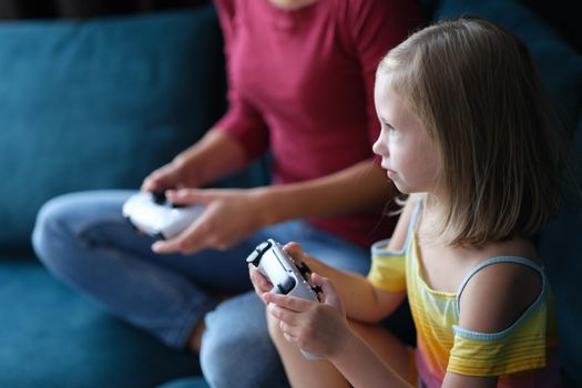 Mom daughter sitting on comfortable sofa and holding joystick. Family playing video games concept