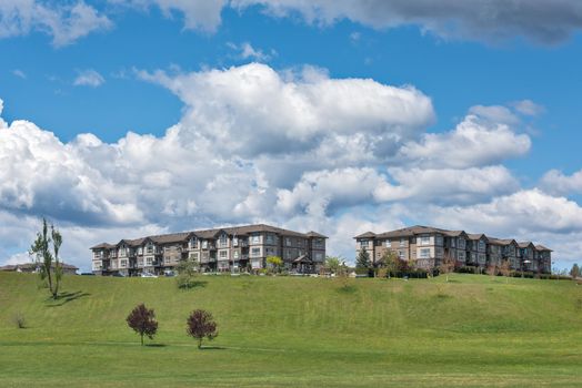 Residential apartment buildings on the hill on cloudy sky background. Green lawn in the park, in front of residential condo building. Residential apartment building on bright sunny day
