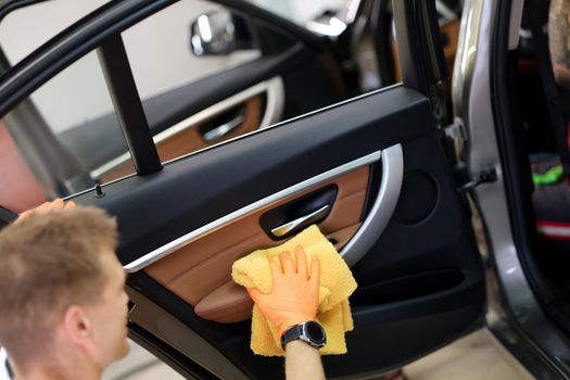 Man cleans car door handle with cloth and car detailing. Car wash services and car interior washing concept