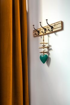 Wooden vintage style hanger with decorative blue heart and red curtain. Hooks on a wall at an entrance to home.