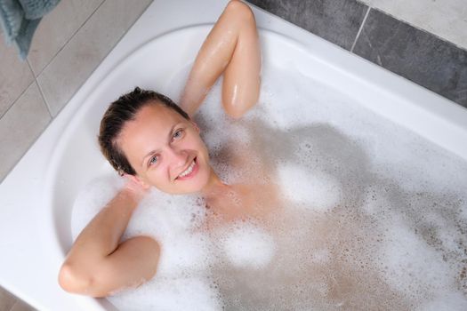 Beautiful young smiling woman lies in bath. Relaxing in bathroom at wellness centre.