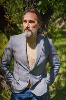 Mature handsome man in 40s 50s in park or yard, away of business or taking a break in warm spring garden outdoors. Handsome grey bearded business man outdoors.