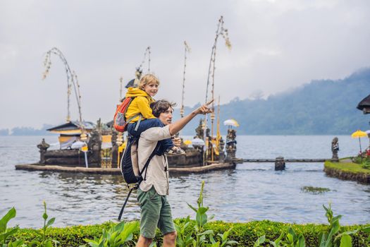 Dad and son in the background of Pura Ulun Danu Bratan, Bali. Hindu temple surrounded by flowers on Bratan lake, Bali. Major Shivaite water temple in Bali, Indonesia. Hindu temple. Traveling with children concept.