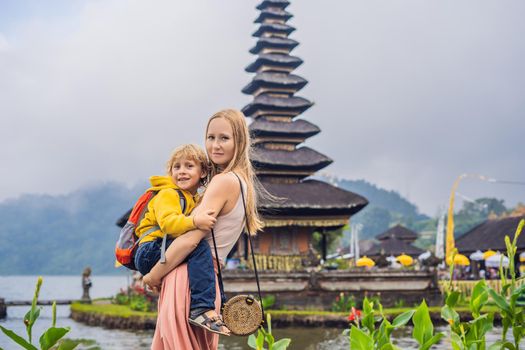 Mom and son in the background of Pura Ulun Danu Bratan, Bali. Hindu temple surrounded by flowers on Bratan lake, Bali. Major Shivaite water temple in Bali, Indonesia. Hindu temple. Traveling with children concept.