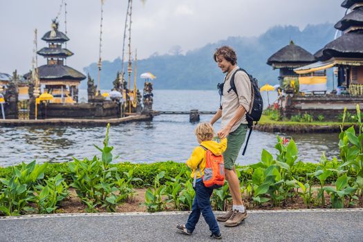 Dad and son in the background of Pura Ulun Danu Bratan, Bali. Hindu temple surrounded by flowers on Bratan lake, Bali. Major Shivaite water temple in Bali, Indonesia. Hindu temple. Traveling with children concept.