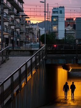 Silhouettes of two persons in an underground crossing, with orange sunset at the background