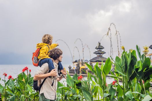 Dad and son in the background of Pura Ulun Danu Bratan, Bali. Hindu temple surrounded by flowers on Bratan lake, Bali. Major Shivaite water temple in Bali, Indonesia. Hindu temple. Traveling with children concept.