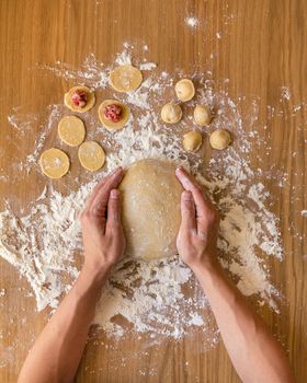 Men's hands holding a ball of dough. Preparation of meat dumplings, several blanks on the wooden table.