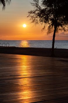 Orange sun rising above the sea. View from promenade with the sea, beach and cafe. The solar path is reflected from pedestrian zone made of wood.