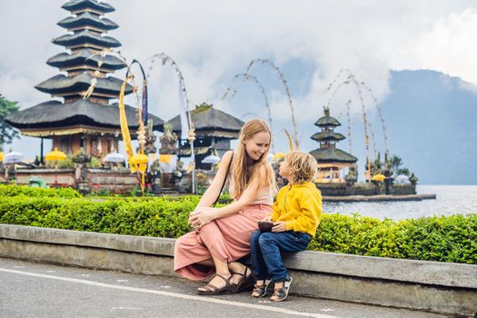 Mom and son in the background of Pura Ulun Danu Bratan, Bali. Hindu temple surrounded by flowers on Bratan lake, Bali. Major Shivaite water temple in Bali, Indonesia. Hindu temple. Traveling with children concept.