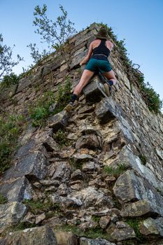 Young brave girl in hat is climbing a ruined building without belay equipment. Adventure spirit, excitement, achievement