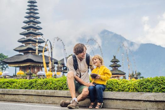 Dad and son in the background of Pura Ulun Danu Bratan, Bali. Hindu temple surrounded by flowers on Bratan lake, Bali. Major Shivaite water temple in Bali, Indonesia. Hindu temple. Traveling with children concept.