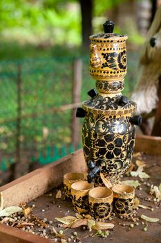 Imitation of traditional russian teapot - samovar with few cups for tea, all made of wood with drawing, on a tray, in a garden