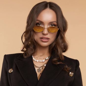 Brunette model with curly hair standing with slightly open mouth. Surprised young girl in sunglasses and black jacket posing on light studio background. Gorgeous lady wearing jewelries on neck.