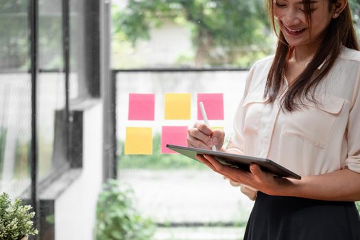 Happy woman manager holding tablet and standing in modern office. Asian female using stylus with tablet.