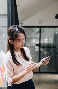 Portrait woman manager holding tablet and standing in modern office. Asian female using stylus with tablet.