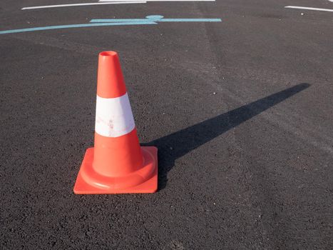 Traffic cone with shadow on asphalt. Traffic cone, with white and orange stripes on gray asphalt, copy space.