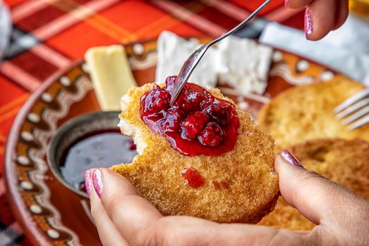 A woman's hand holds a fried slice of bread with jam at breakfast.