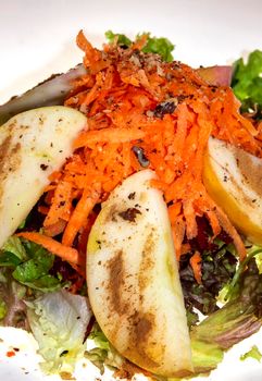 Fresh salad with lettuce, carrots, red beets, chopped apples with dressing in a ceramic plate. Vertical view