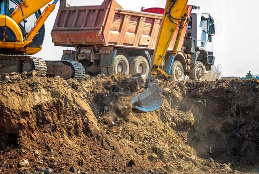 Excavator is loading excavation on the truck. Heavy construction equipment consisting of a boom, dipper or stick, bucket, and cab on a rotating platform.