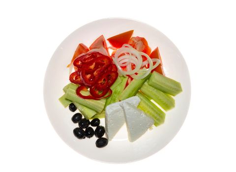 Traditional Greek salad. Tomatoes, sliced cucumbers, paprika, onion, black olives, cheese in ceramic plate, isolated on white background. Top view