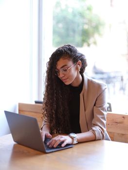 woman with her hair to one side sitting using her laptop in a cafeteria, light saturated vertical background