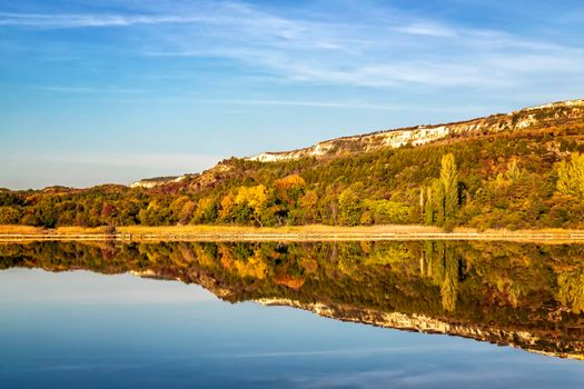 Colorful tree line on a calm lake at sunrise during autumn.