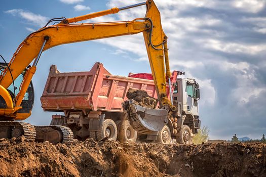 Yellow excavator and empty dump truck working at the construction site
