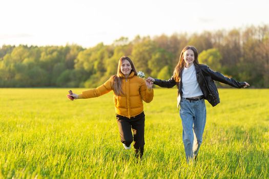 Mom and daughter casual dressed run in field at beautiful spring sunset. Mothers love concept.
