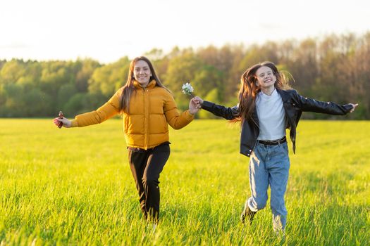 Mom and daughter casual dressed run in field at beautiful spring sunset. Mothers love concept.