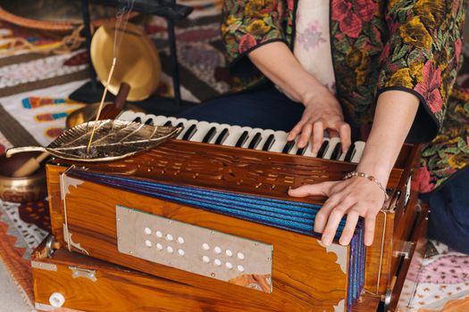 Hands of a woman sitting on the floor and playing the harmonium during the practice of kundalini yoga.