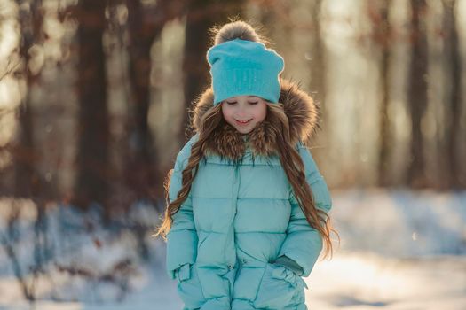 girl in a jacket and hat of turquoise color against the backdrop of a snowy forest