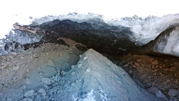 Ice cave in the snowy mountains. Tuyuk-Su glacier. Black ice reflects everything like a mirror. The ledge of stones collapsed. huge cracks in the ice tunnel. Snowy mountains of Almaty, Kazakhstan.