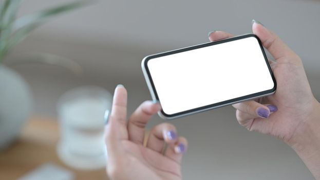 Close up view woman holding smart phone in horizontal position with empty screen for graphics display montage.