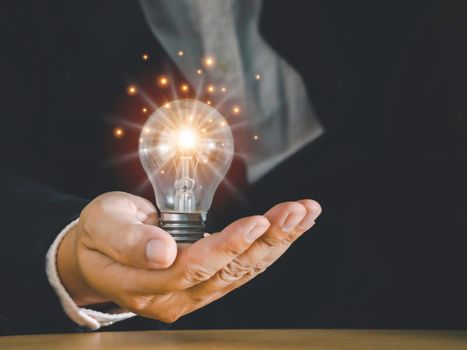 Hand of businessman holding light bulb with fire spark shine glitter for new idea with innovation and inspiration, communication and technology in science concept.