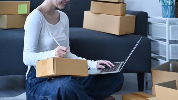 Start up small business entrepreneur confirming orders from customer on laptop and preparing parcel boxes for delivery.