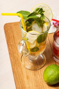 Cold refreshing summer lemonade mojito with lemon slices and mint in a tall glass and strawberry lemonade with mint in a short one on wooden cutting board. Top view.