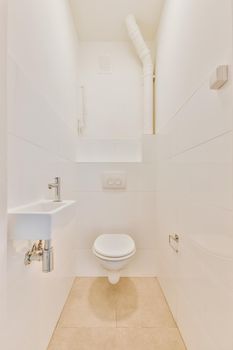 Wall hung toilet and small sink in corner in lavatory room with beige tile