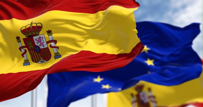 Detail of the national flag of Spain waving in the wind with blurred european union flag in the background on a clear day. Democracy and politics. European country. Selective focus.