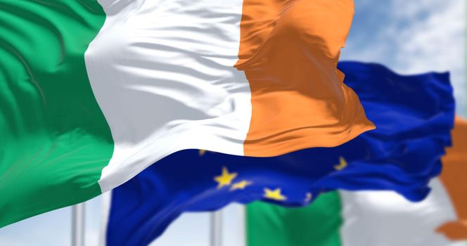 Detail of the national flag of Ireland waving in the wind with blurred european union flag. In the background on a clear day. Democracy and politics. European country. Selective focus.