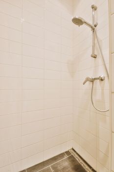 Shower faucets attached to tiled wall near glass partition and ornamental curtail in washroom at home