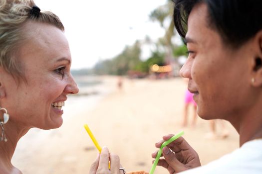 Close up view of lovers looking to each other while sharing a coconut juice in the beach