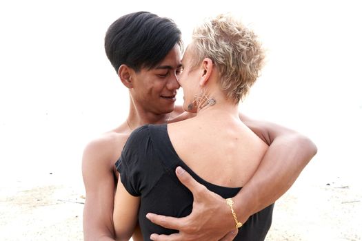 Multiethnic couple looking each other tenderly while embracing on a beach at sunset