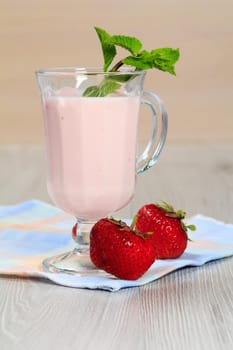 Glass of delicious yogurt with mint and fresh strawberries on white wooden table