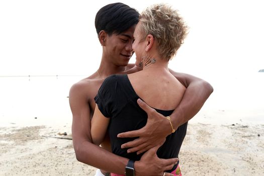 Multcultural couple looking each other tenderly while embracing on a beach at sunset